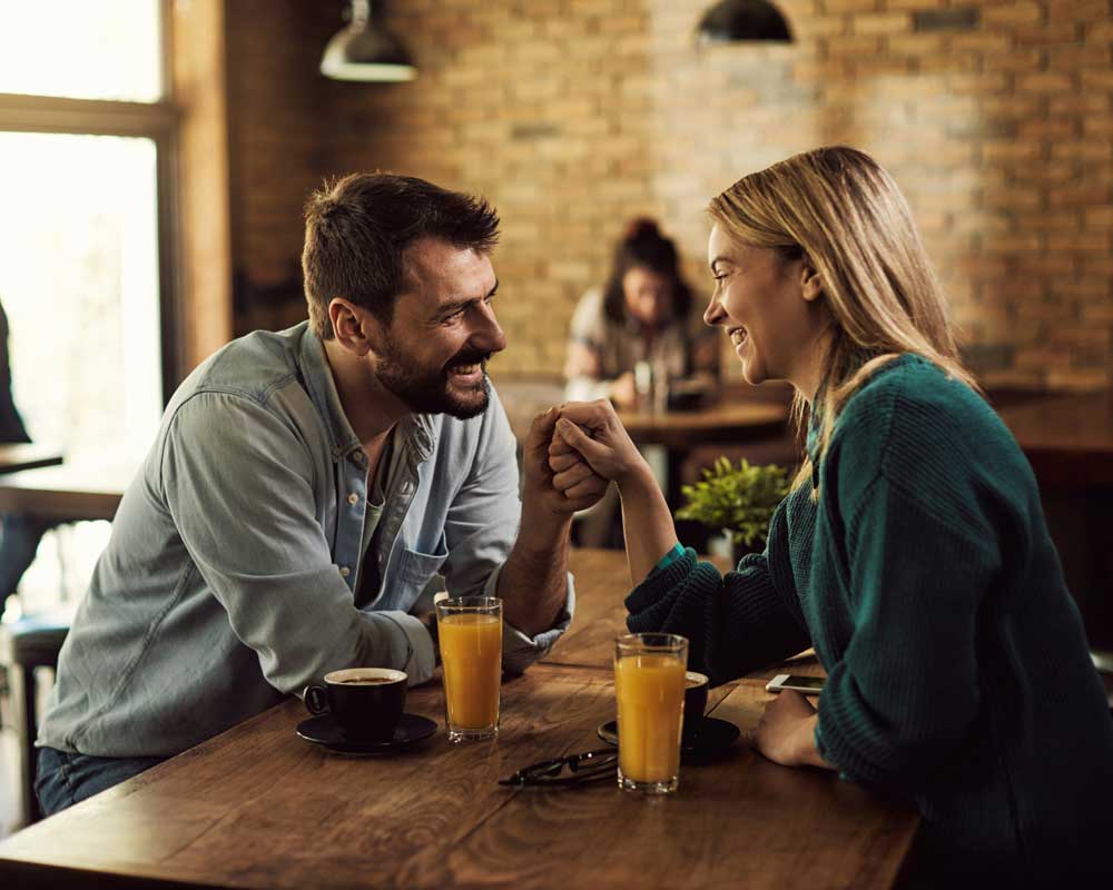 A Canadian couple at a cafe, having smoothies, talking about their finances together, including which is the best bank account for them to use.