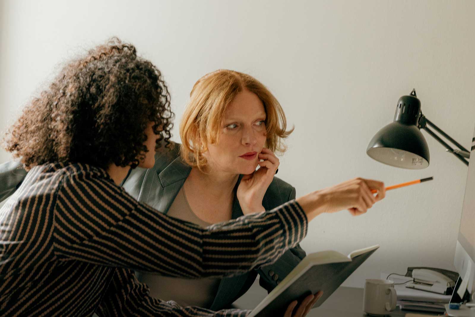 Two Canadian women, looking at a computer and doing long-math calculations on paper, debating if you need $1.5 million to retire.