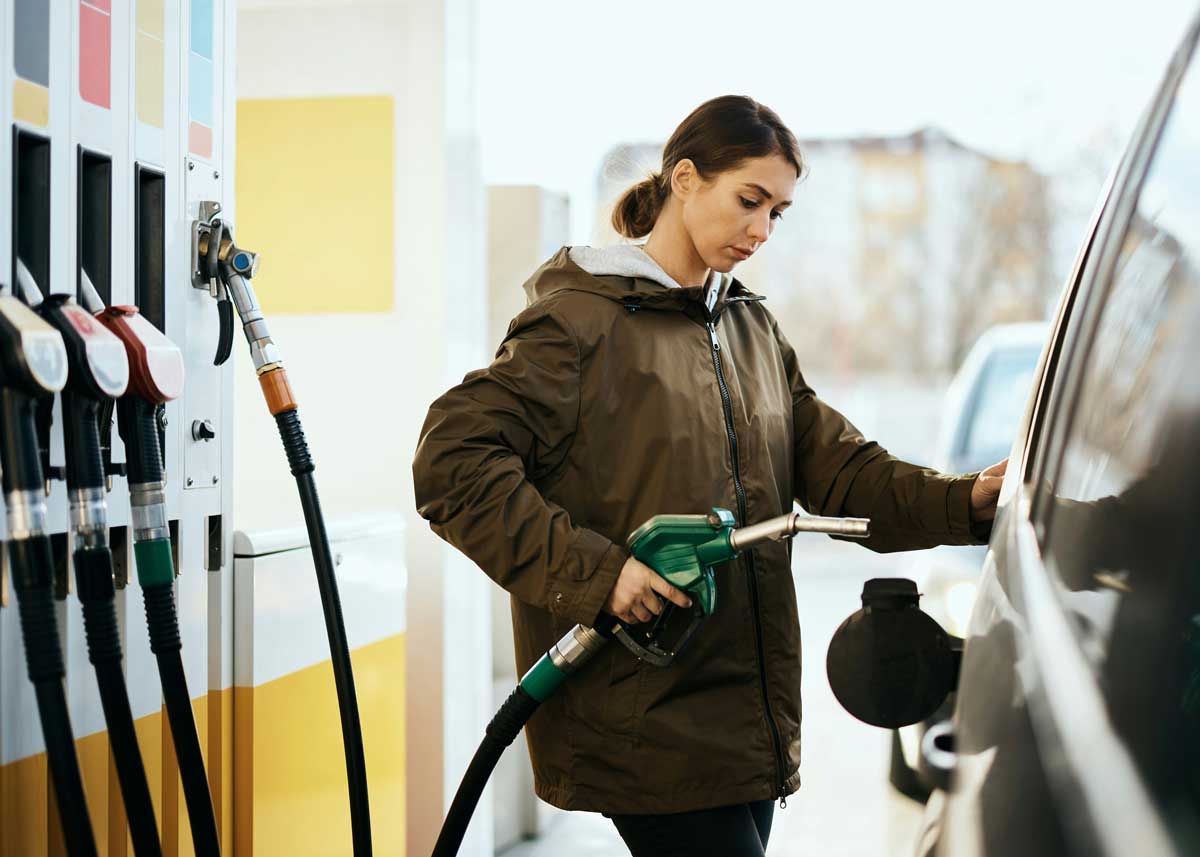 A Canadian woman filling her tank at the gas station, wondering to herself at the pump about how to predict gas prices.