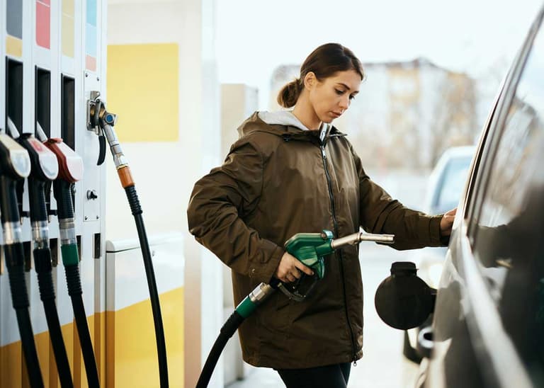 A Canadian woman filling her tank at the gas station, wondering to herself at the pump about how to predict gas prices.
