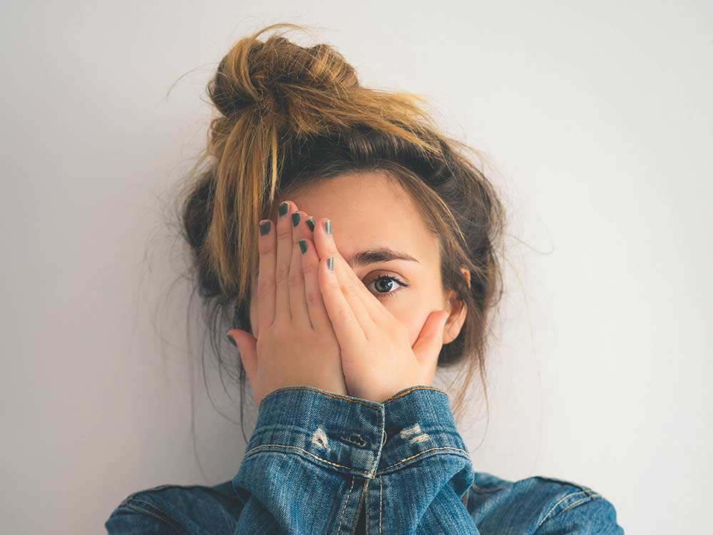 A Canadian woman hiding behind her hands, symbolizing fear of debt in Canada.