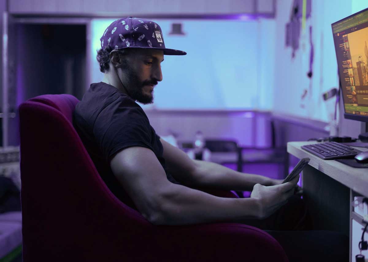 A Canadian man looking at his desktop gaming computer and his gambling app, wondering what the costs are for his habit.