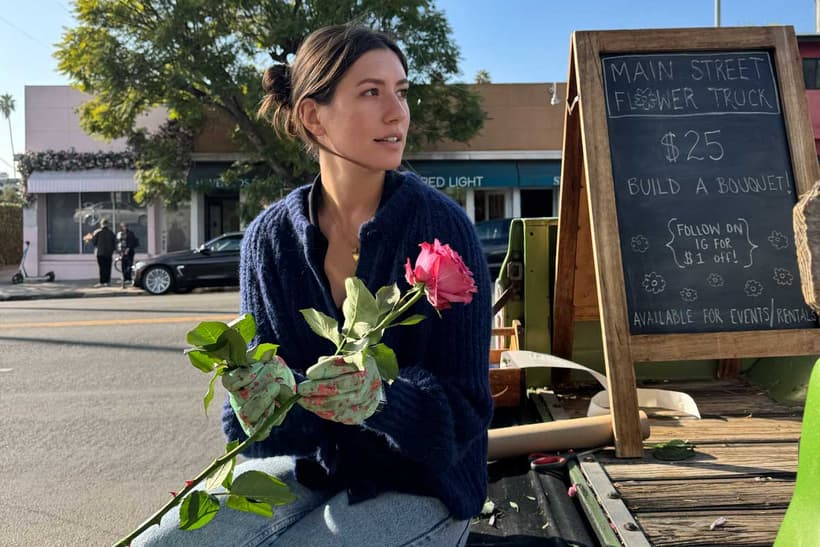 Vienna Hintze holding a flower, as she trims a rose stem in the back of her flower truck.