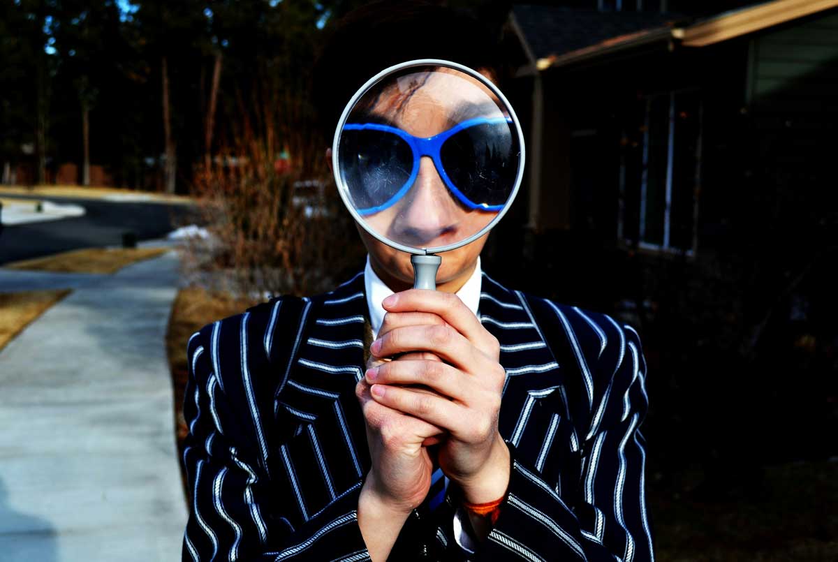A Canadian with a magnifying glass, to symbolize searching for old accounts and missing money with the Bank of Canada.