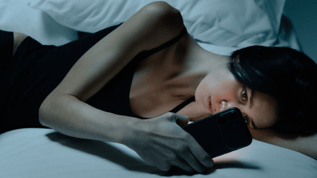 A stressed person laying in bed with a smartphone in hand, searching for bankruptcy alternatives for Canadians struggling with debt