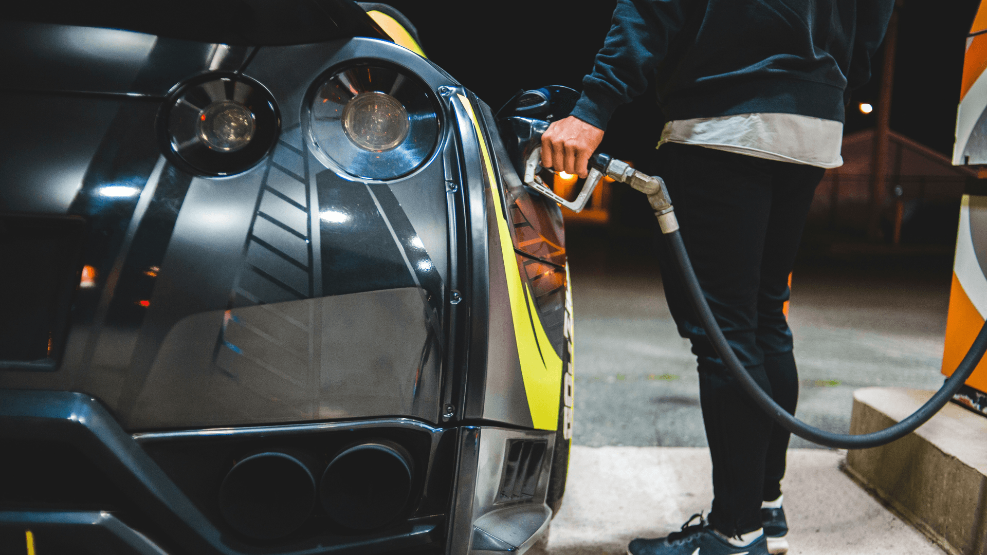 A person pumping fuel into a sleek black car at a gas station pump at night, showcasing a scenario where using the best no-fee gas credit cards in Canada for fuel cashback can maximize savings.