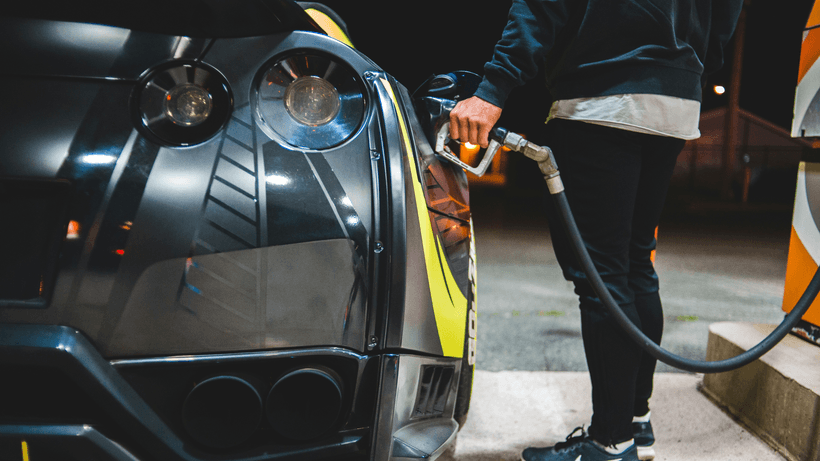 A person pumping fuel into a sleek black car at a gas station pump at night, showcasing a scenario where using the best no-fee gas credit cards in Canada for fuel cashback can maximize savings.