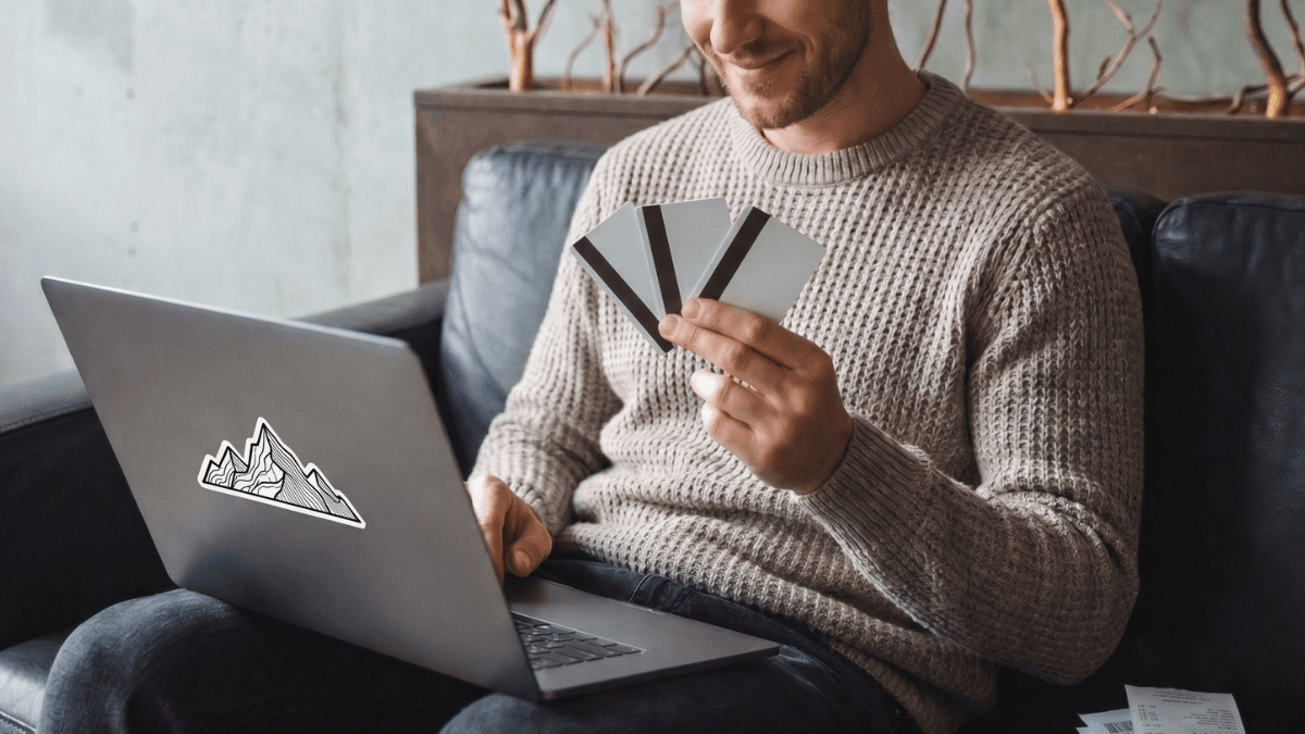 A Canadian using their laptop and comparing three different types of credit cards—an unsecured credit card, secured credit card and prepaid card—before making a purchase.