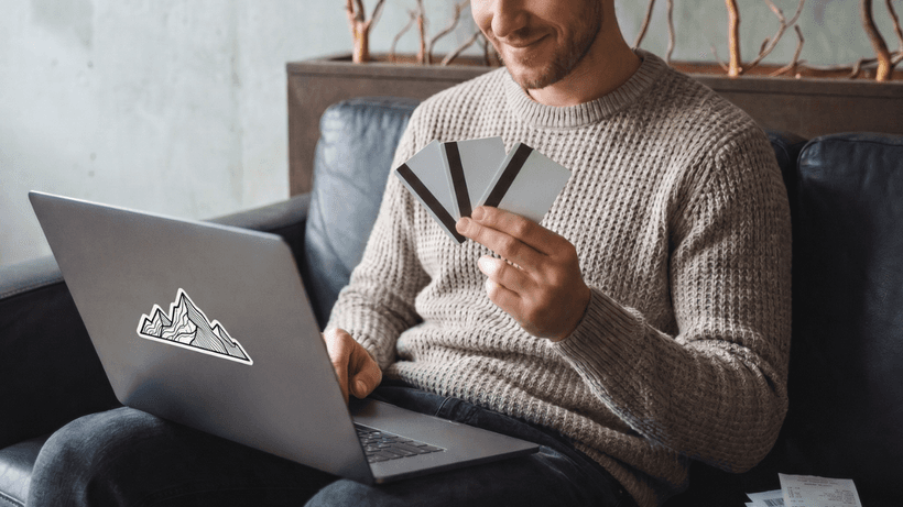 A Canadian using their laptop and comparing three different types of credit cards—an unsecured credit card, secured credit card and prepaid card—before making a purchase.