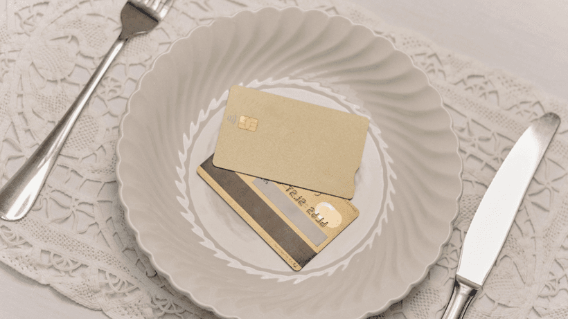 Two credit cards on a ceramic plate, between a set of utensils—a visual representation of the question: Does paying your credit card twice a month help with your credit score?