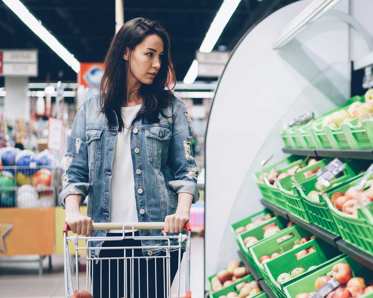 A Canadian woman looking at the prices of food at the grocery store, wondering if any relief on gas costs will help make groceries more affordable.