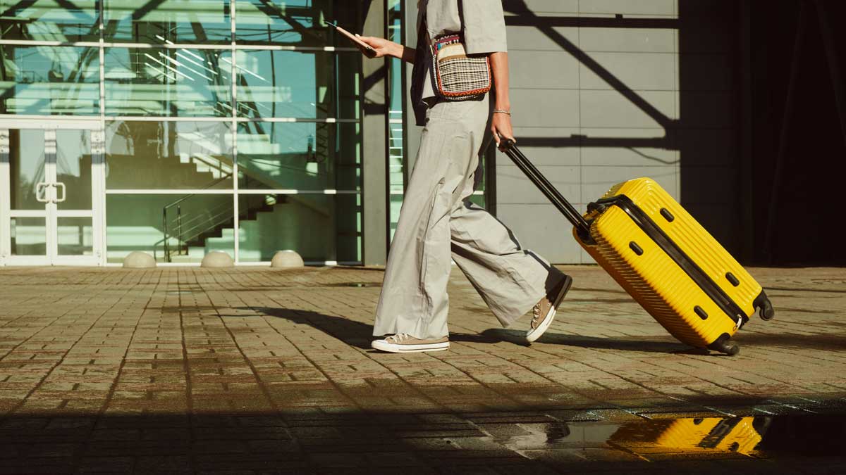A Canadian with her rolling suitcase, checking in on her phone, while also looking at if she can save on baggage fees.
