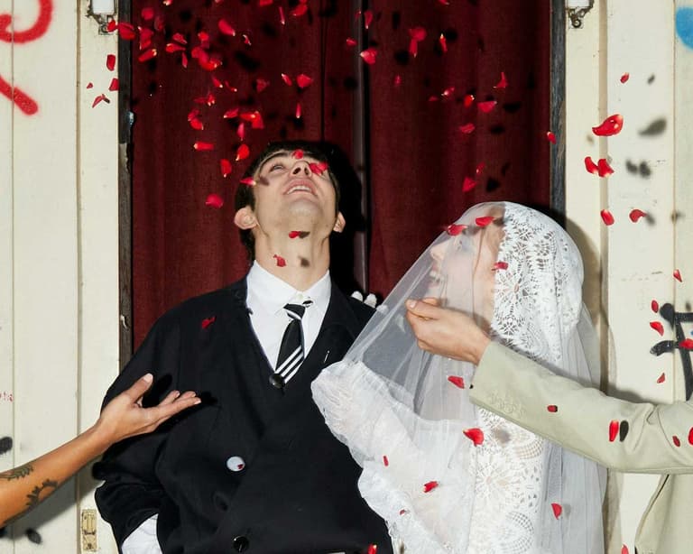 A couple on their wedding day, as family and friends throw petal confetti, in addition to giving money gifts.