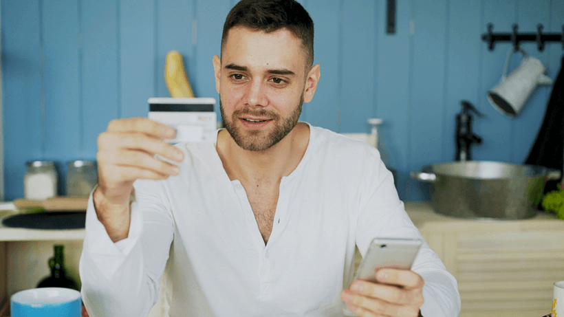 A person holding a credit card in one hand and a smartphone in another as they search how to boost your credit score fast in Canada