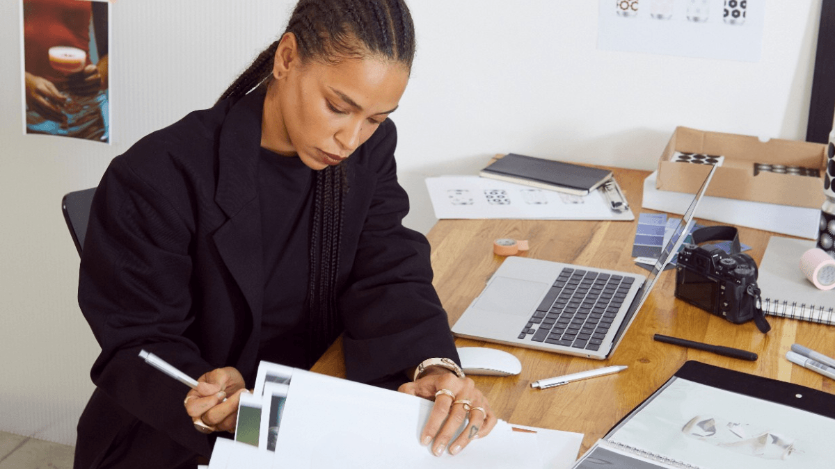 A person with a pen in hand, sifting through a pile of papers on a work desk, as they figure out how to choose a credit card in Canada