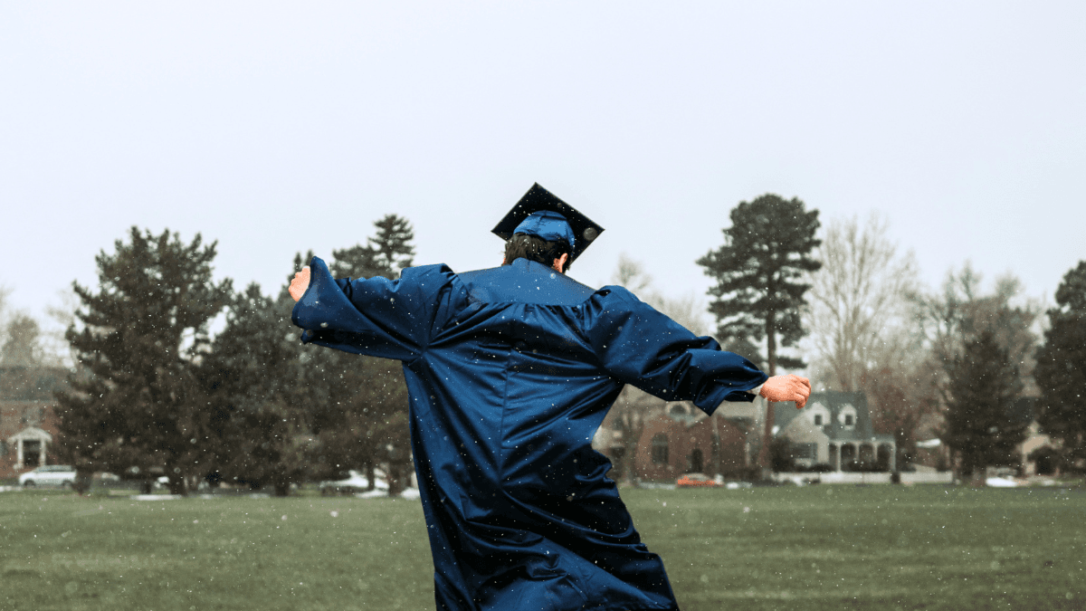 A person wearing a graduation gown and cap, celebrating on an open field, symbolizing the process of how to graduate from a secured credit card to an unsecured credit card in Canada.