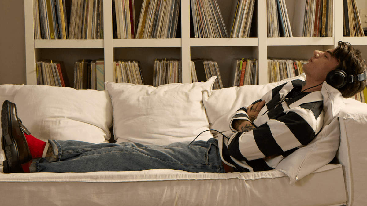 A person, laying on a couch in front of shelves stacked with books and magazines, thinks about how they can keep their house while going through a consumer proposal in Canada