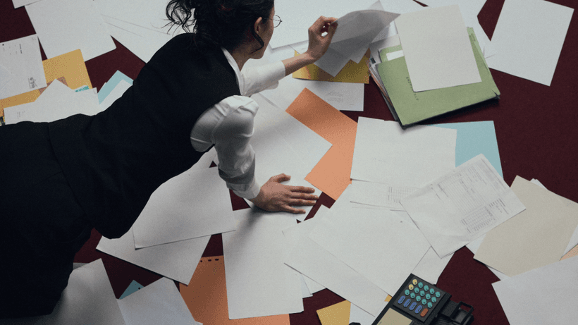 A person leaning over a pile of tax paperwork, attempting to figure answer if interest on savings accounts in Canada is taxable