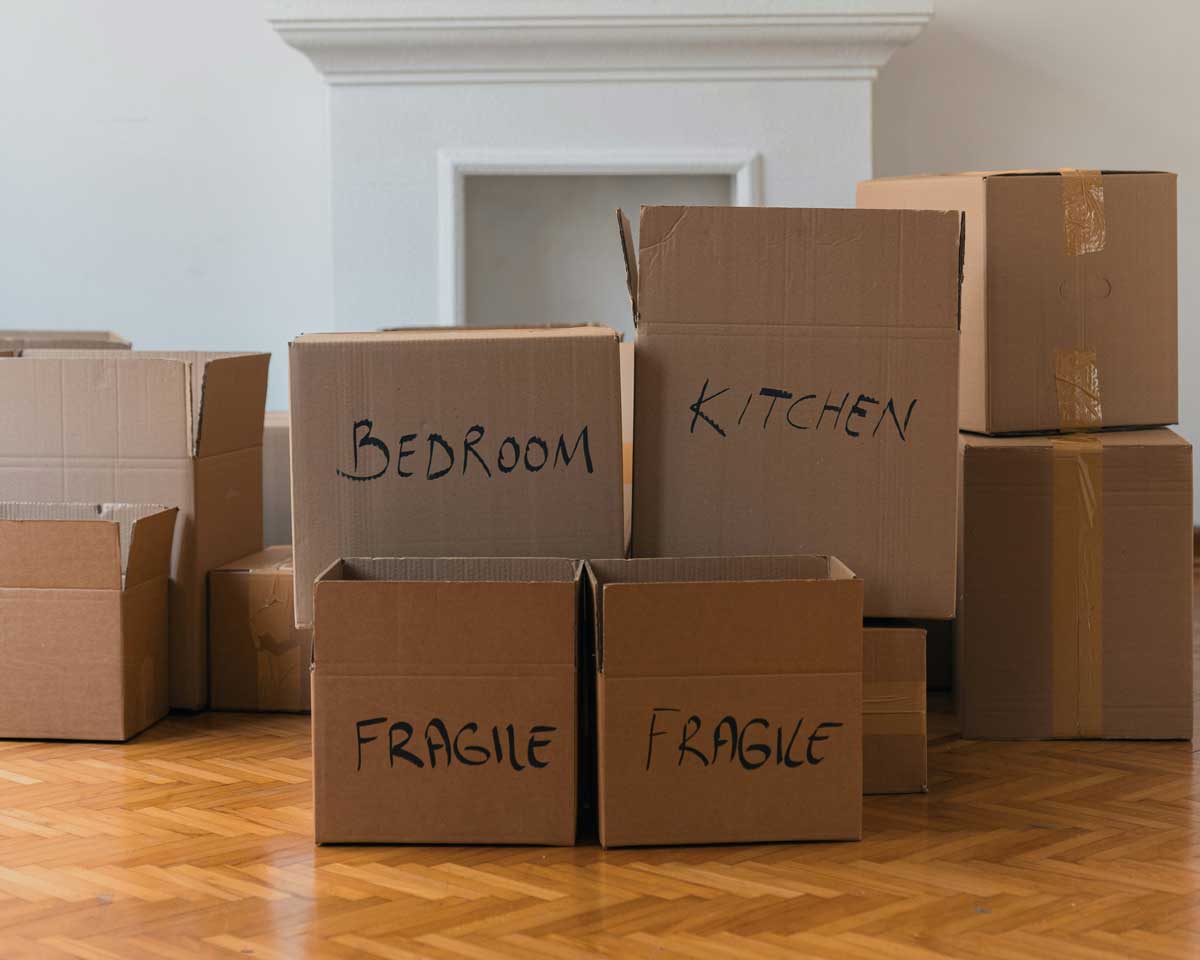 A Canadian summer lit living room, with moving boxes piled in front of a fire place.