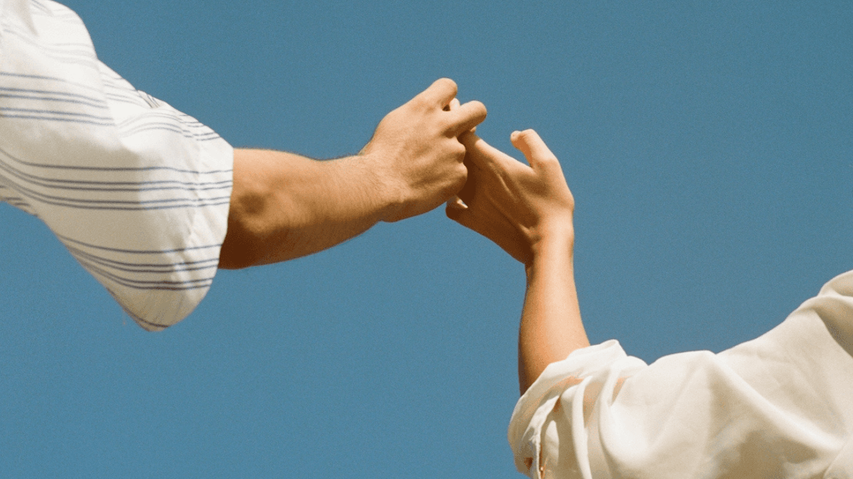 Two people holding hands against the sky, symbolizing the importance between communicatoin, couples and money