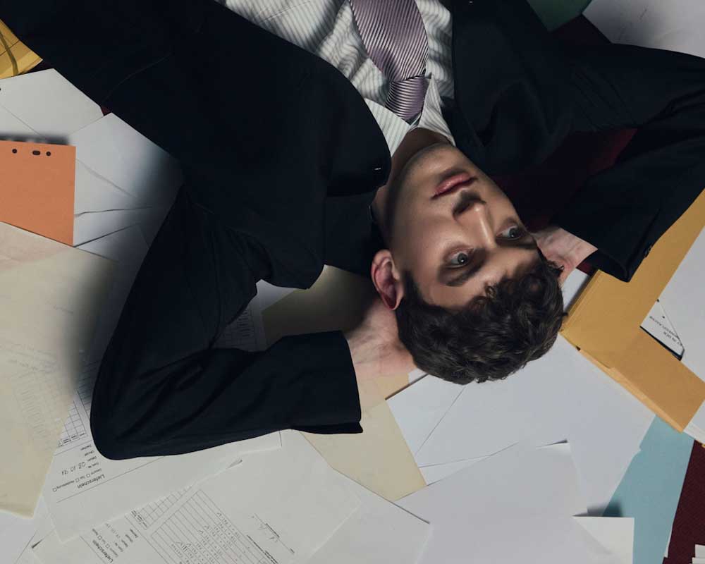 A young Canadian man, dressed for work, but laying on a bunch of files, relaxing, as he makes money with little effort.