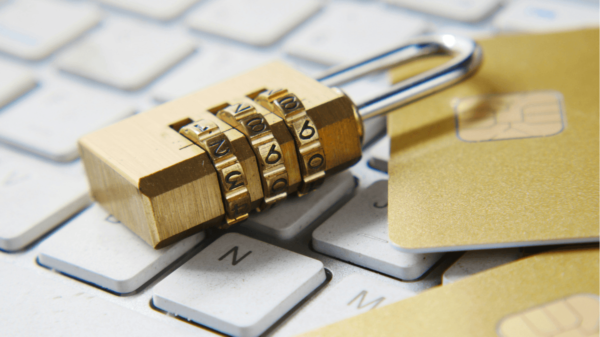 A gold combination padlock resting on a computer keyboard next to gold credit cards, representing secured credit cards in Canada.