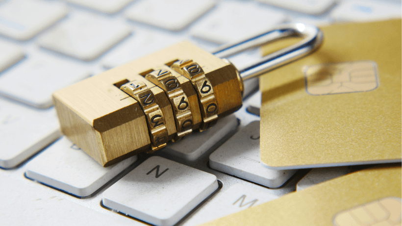 A gold combination padlock resting on a computer keyboard next to gold credit cards, representing secured credit cards in Canada.