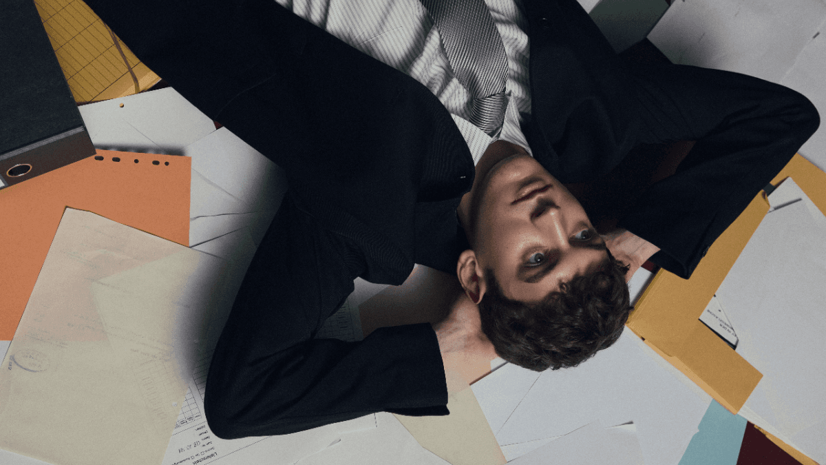 A businessman lying upside down on a pile of scattered paperwork, wondering what a statement balance means on a credit card statement