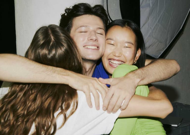 Three Canadians hugging and smiling. The World Happiness Report shows Canada has dipped in rankings. What does money have to do with it?